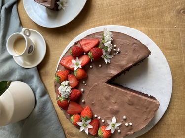 Erdbeer-Brownie-Torte angeschnitten, daneben Kaffeetasse und Teller mit Tortenstück