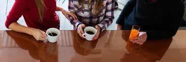 3 Personen mit Kaffeetassen an einem Tisch