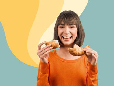 Eine lachende Frau mit einem zerteilten Croissant in den Händen
