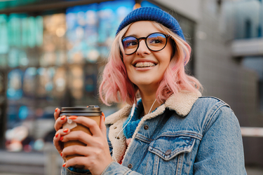 Lächelnde Frau hält Kaffeebecher mit beiden Händen