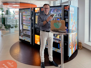 Fritz Kaltenegger mit einem "too good to go"-Sackerl, im Hintergrund Snack- und Getränkeautomaten