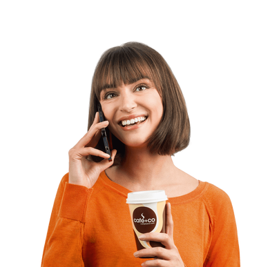 Eine lachende Frau spricht am Smartphone und hält einen Kaffeebecher in der Hand