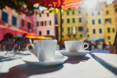 Zwei Tassen Kaffee auf einem Tisch, im Hintergrund ein Platz mit bunten Häuserfronten