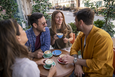 Zwei Frauen und zwei Männer lachend an einem Kaffeehaustisch mit Kaffeetassen