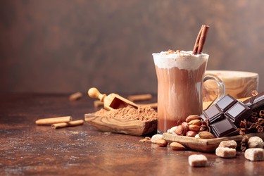 Kaffee mit Schlagobers und Zimstange, Schokolade, Nüsse und Gewürze daneben verstreut