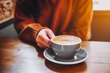Frau sitzt an einem Holztisch mit einer großen Tasse Kaffee mit Milchschaum