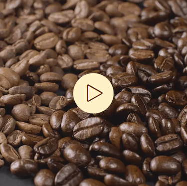 Kaffeebohnen bildfüllend, im Vordergrund ein Symbol zum Abspielen von Videos
