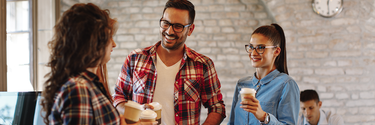 Zwei Frauen und ein Mann mit Kaffeebechern bei einer fröhlichen Unterhaltung im Büro