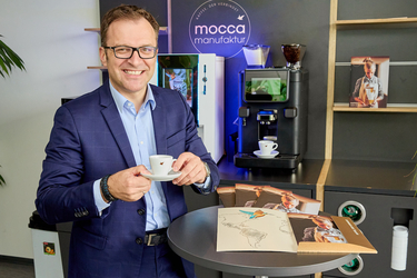 Fritz Kaltenegger mit Kaffeetasse, im Hintergrund Kaffeemaschinen und café+co Werbematerial